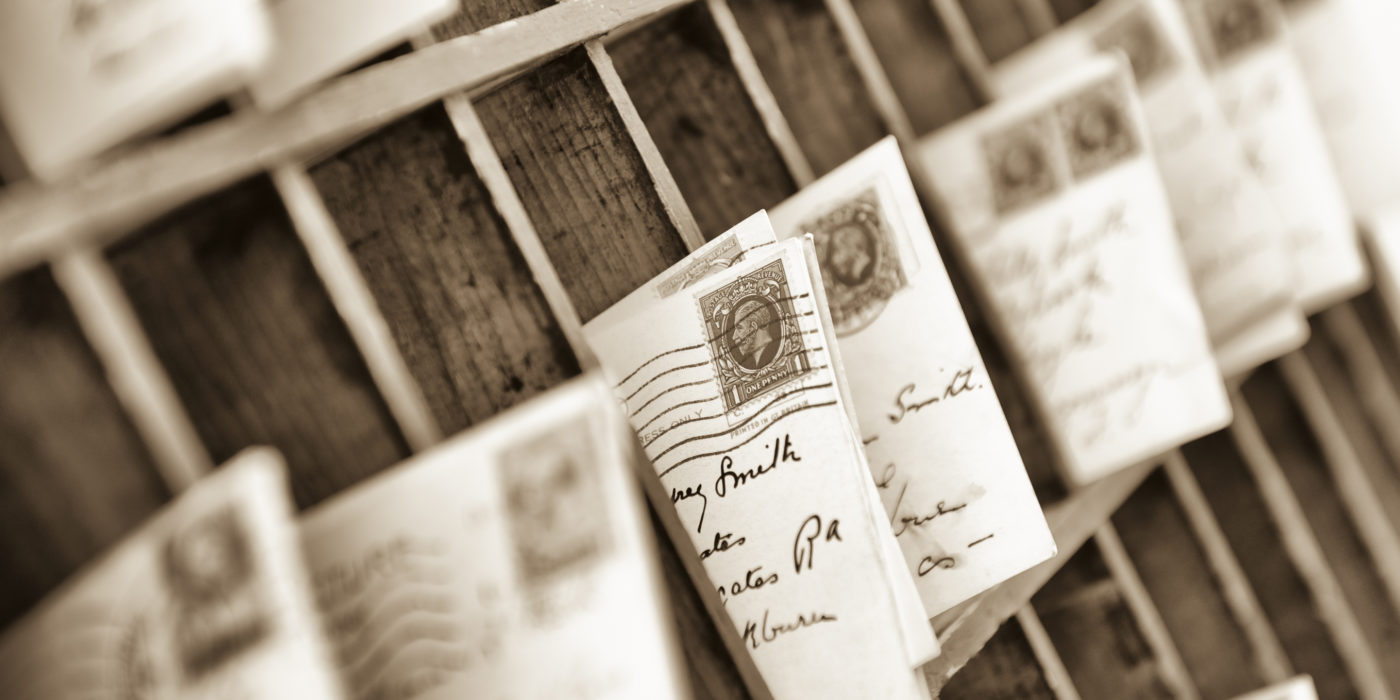 old fashioned letters and postcards sorted into old fashioned wooden mail box slots. 1930s postmarked British stamp at frame centre.